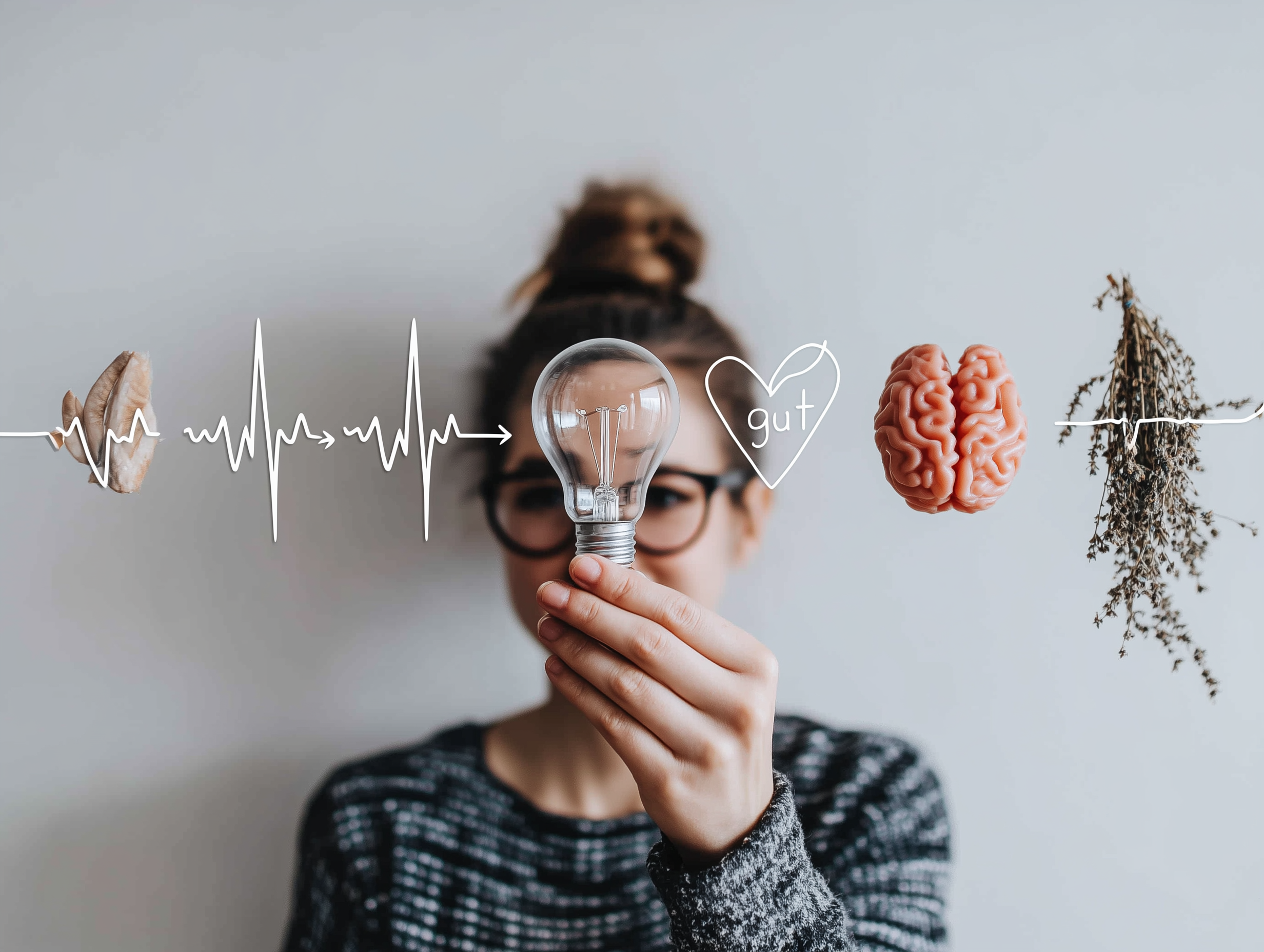 Person holding a lightbulb with illustrated heartbeat line, heart with the word gut, brain, and herbs, symbolising finding the root cause of symptoms and holistic health insights.