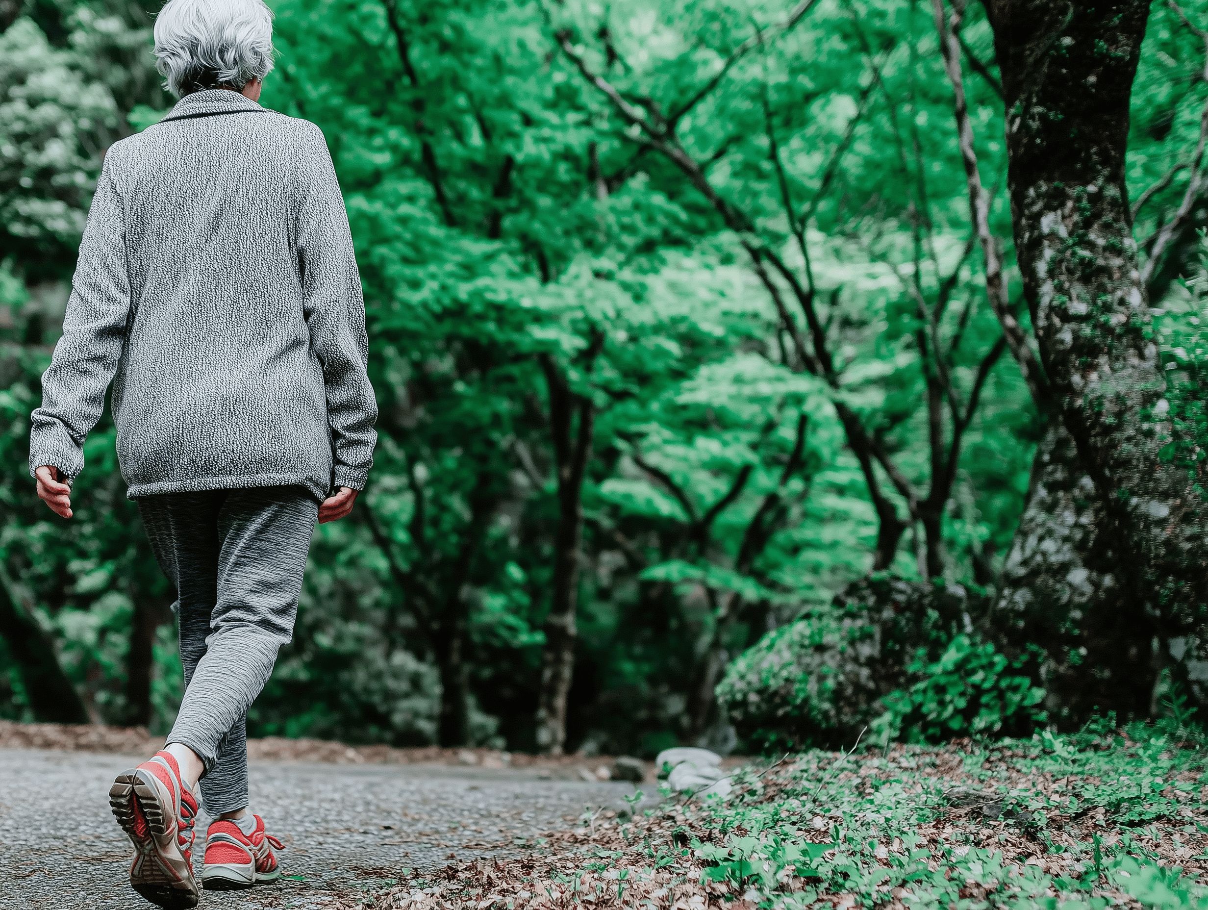 Person walking slowly along a tree-lined path in a green park, wearing casual grey clothes and red trainers, symbolising gentle daily movement for better health